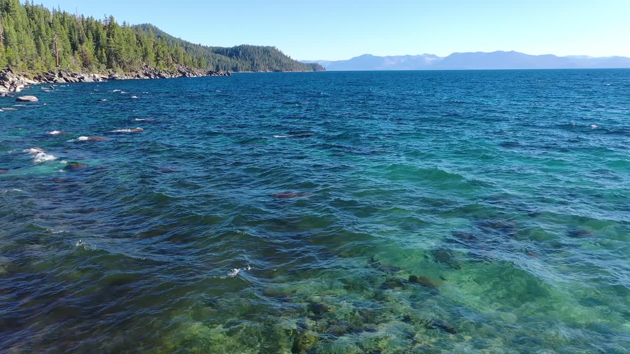 캘리포니아 시에라 네바다 산맥에 있는 화려한 꽃 수영복을 입고 타호 호수 해변에 서 있는 아름다운 여성 위로 드론 비행