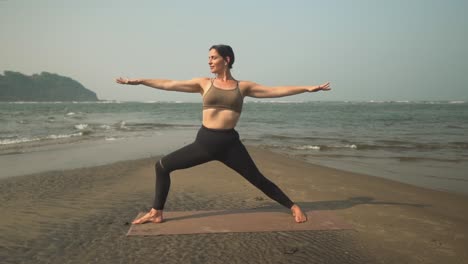 Pose-De-Yoga-Guerrera,-Mujer-Virabhadrasana-Ejerciendo-Estiramientos-En-El-Mar-De-La-Playa-Al-Aire-Libre