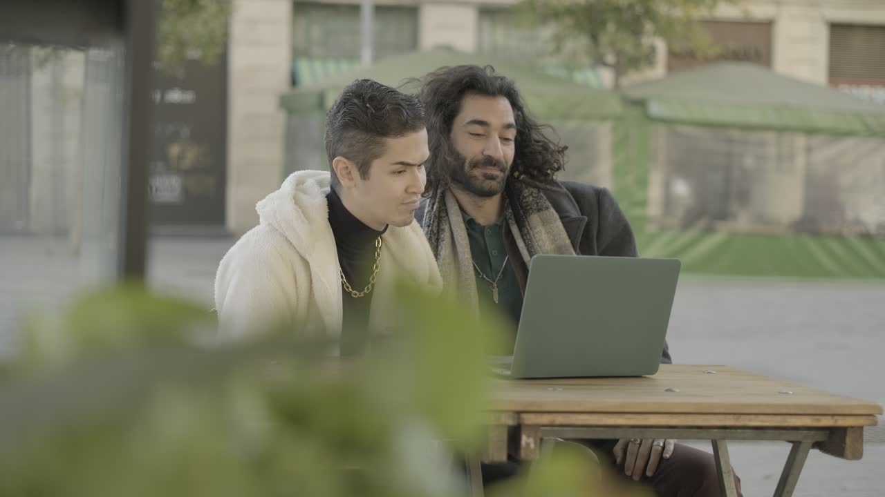 Two men working on a laptop at an outdoor cafe