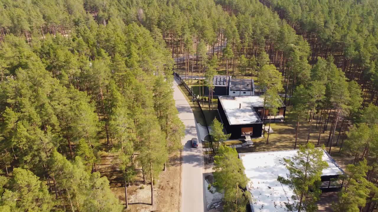A car drives through a lush green forest, passing cozy houses for a relaxing stay—seen from above.