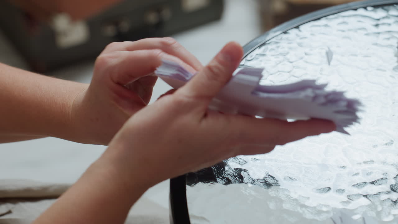 close hand view arranging paper crafts neatly on glass table preparing handmade ornaments delicate fingers organizing sharp cut shapes during festive art project indoors cozy atmosphere