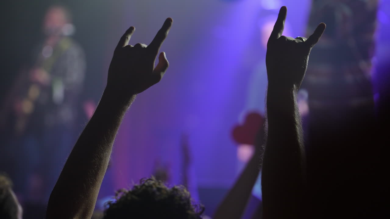 Rock and roll fans expressing intense excitement during live music performance, raising hands with iconic devil horns gesture, embodying raw energy and passion of concert atmosphere