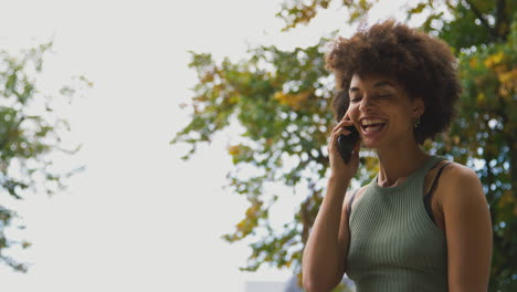 smiling young woman outdoors laughing as she talks on mobile phone