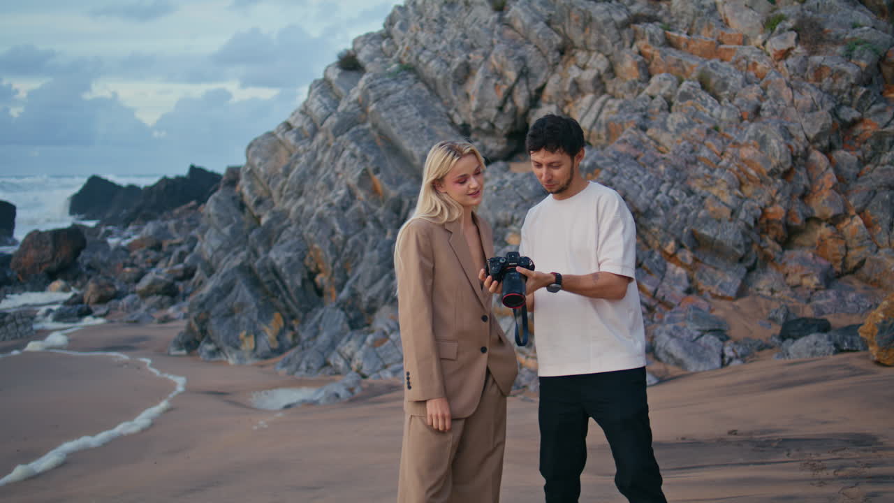 профессиональный фотограф показывает фотографии с камеры на скалистом пляже.