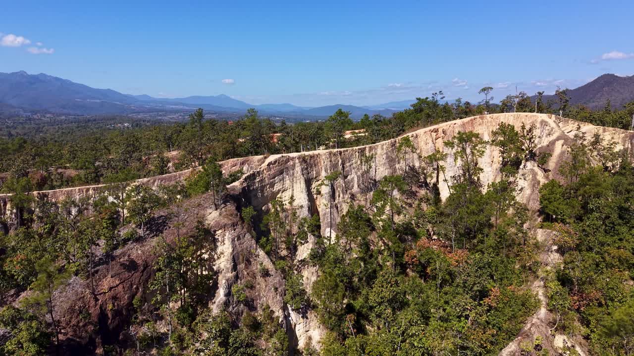 Rivelazione aerea con drone del Canyon di Pai nel Nord della Thailandia, che mostra aspre creste rosse e sentieri escursionistici, con catene montuose distanti all'orizzonte sotto un cielo azzurro limpido e una lussureggiante foresta verde circostante