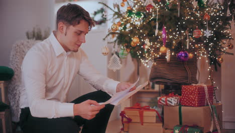 happy man reading letter by christmas presents and decorated tree