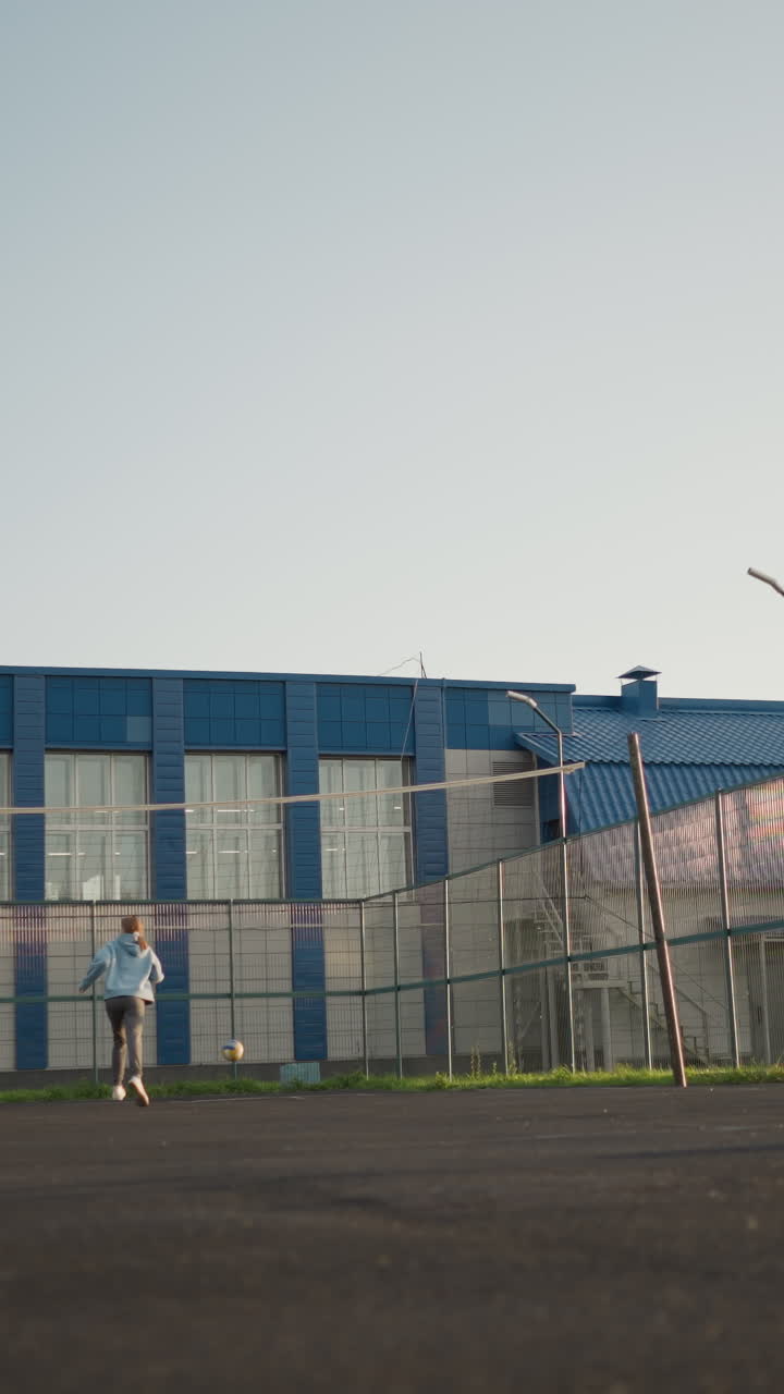 en la cancha de voleibol, la dama de leggings verdes sirve la pelota mientras la dama de capucha azul se apresura a atraparla, otras dos mujeres están de pie en el fondo, con el edificio visible