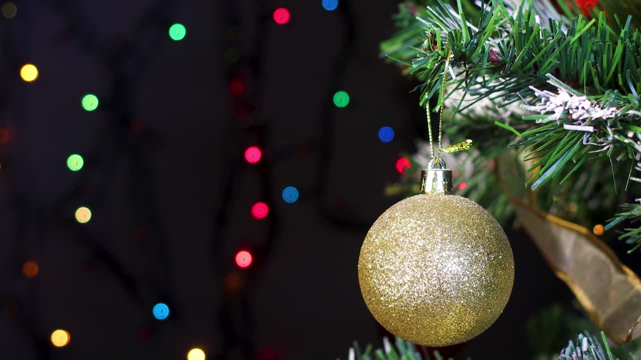 ornamento de brillo dorado en el árbol de navidad con luces de colores parpadeantes detrás