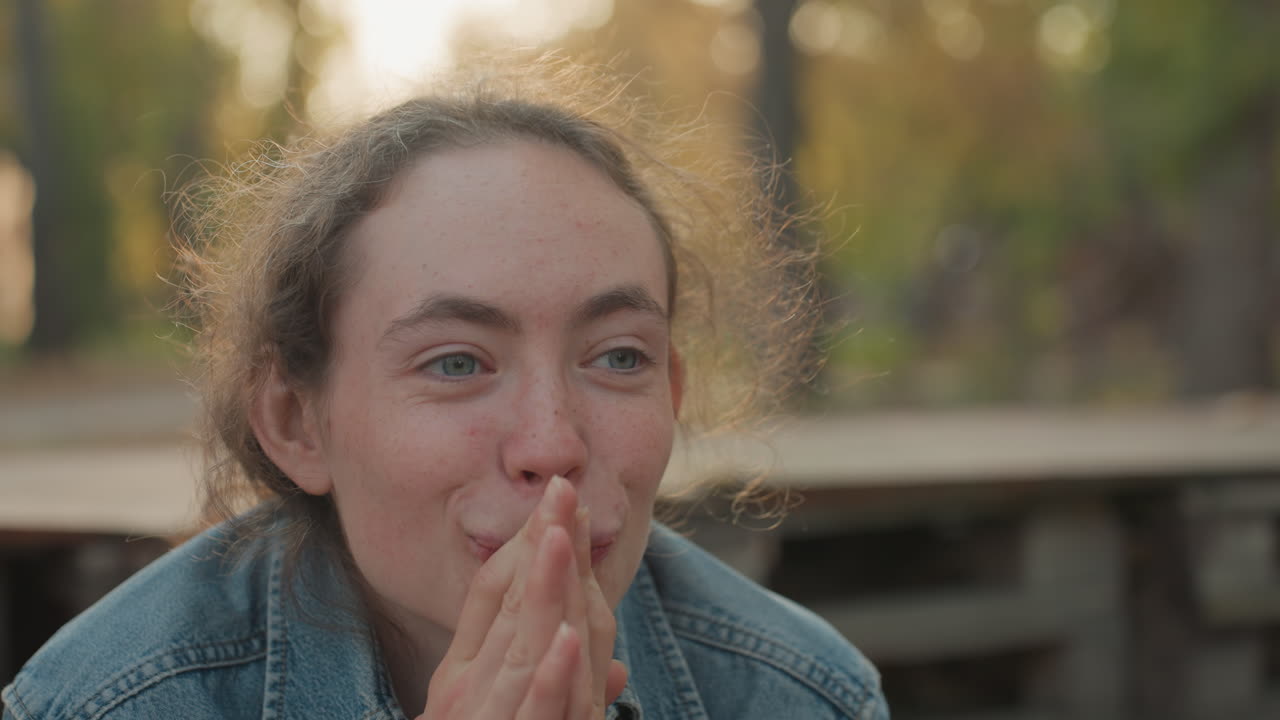 Kvinne i denim reagerer med gledelig forventning på en utendørsbenk ved solnedgang, hendene knyttet nær munnen, lekent smil, tårevåte øyne, varmt høstlys, ærlig portrett som fanger intimt ekteskap og familie.