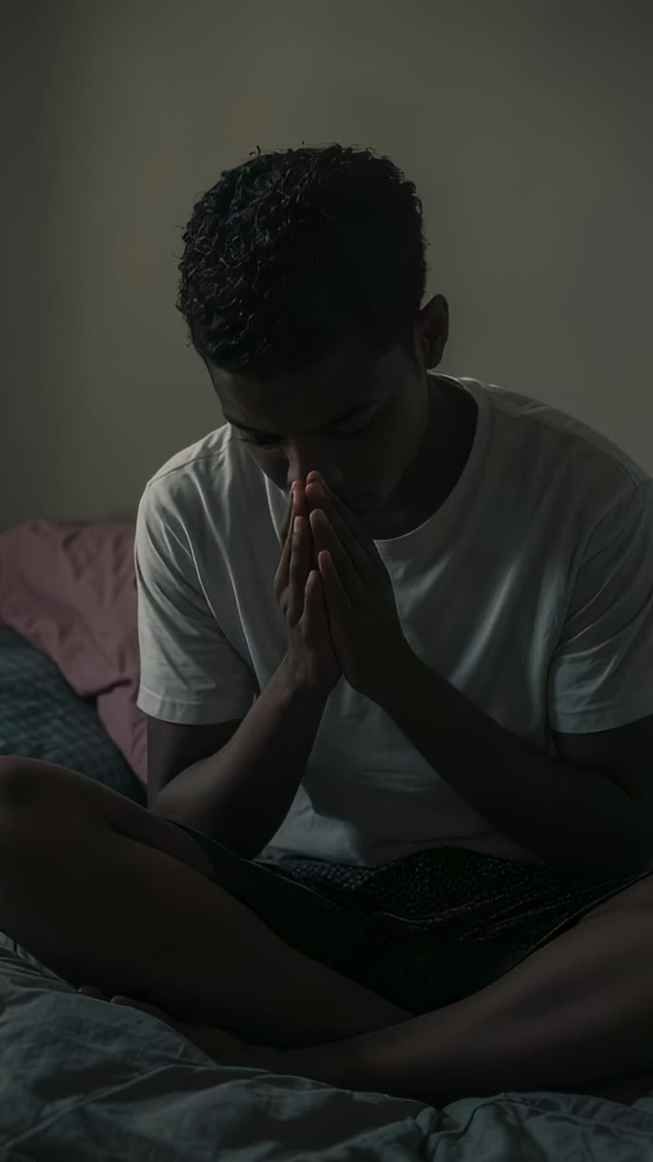 Vídeo vertical: adolescente, de pernas cruzadas na cama e vestindo uma camiseta branca, levanta a cabeça após orar e fala para a câmera