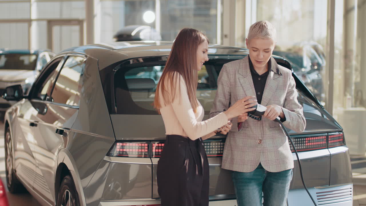 mujeres comprobando el puerto de carga de automóviles eléctricos en el concesionario