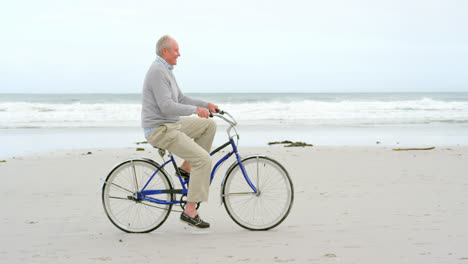 Side-view-of-old-caucasian-senior-man-riding-bicycle-at-beach-4k