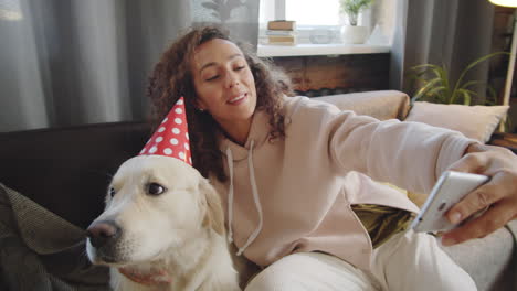 woman taking selfie with dog wearing party hat