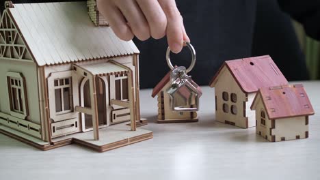 llavero con las llaves del apartamento en la mano. casas de juguete en la mesa. compra de bienes raíces. transacción inmobiliaria