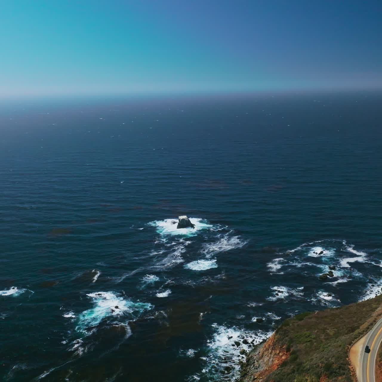 Rocky shore with highway over cliffs. Beautiful endless blue Pacific Ocean interflowing with clear azure sky. Aerial view