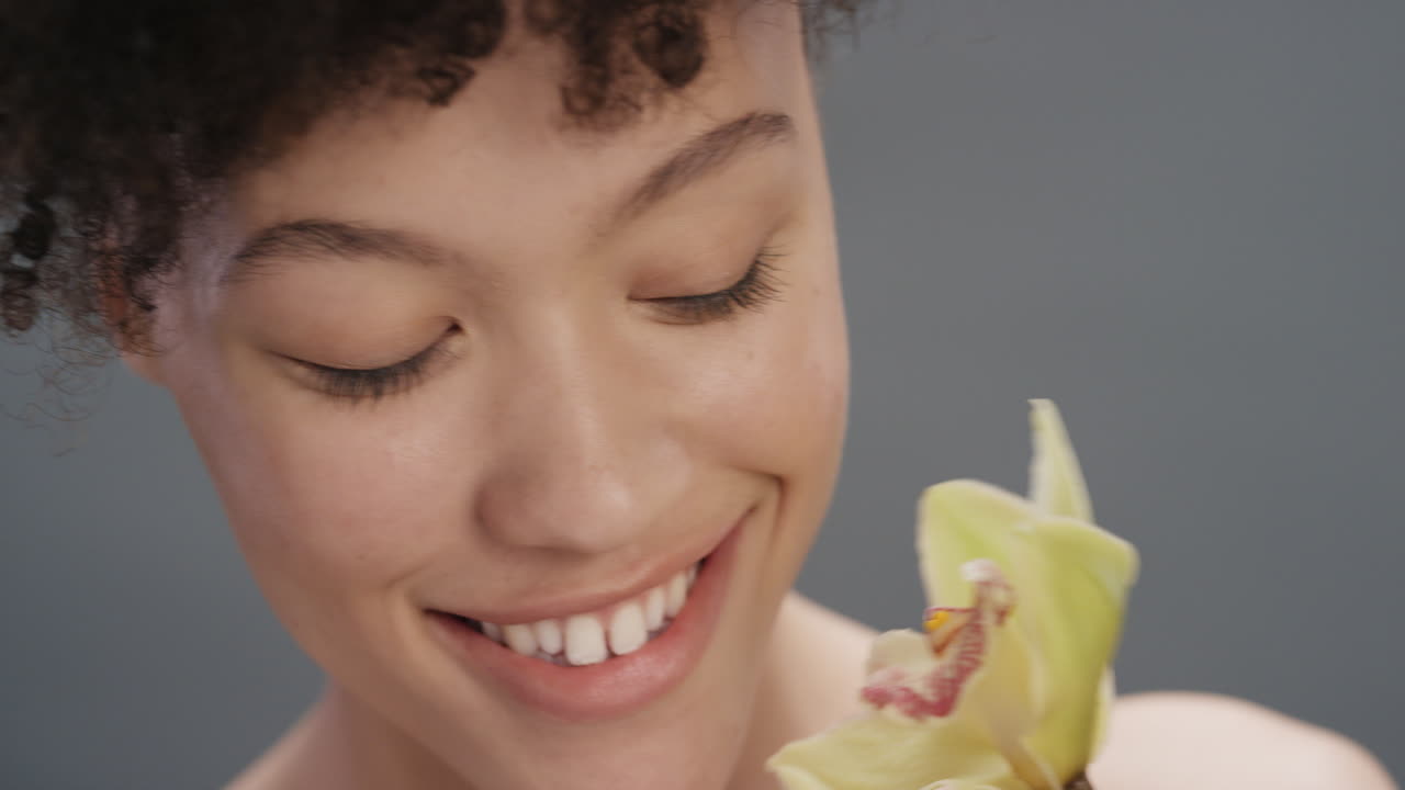 ritratto ravvicinato bellezza donna che tocca la pelle con fiore d'orchidea accarezzando pelle liscia sana godendo di fragranza naturale sensuale flirtosa giovane donna su sfondo grigio concetto di cura della pelle