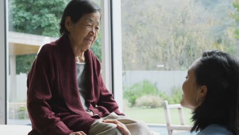 Smiling-asian-female-physiotherapist-treating-knee-of-senior-female-patient-and-talking-at-surgery