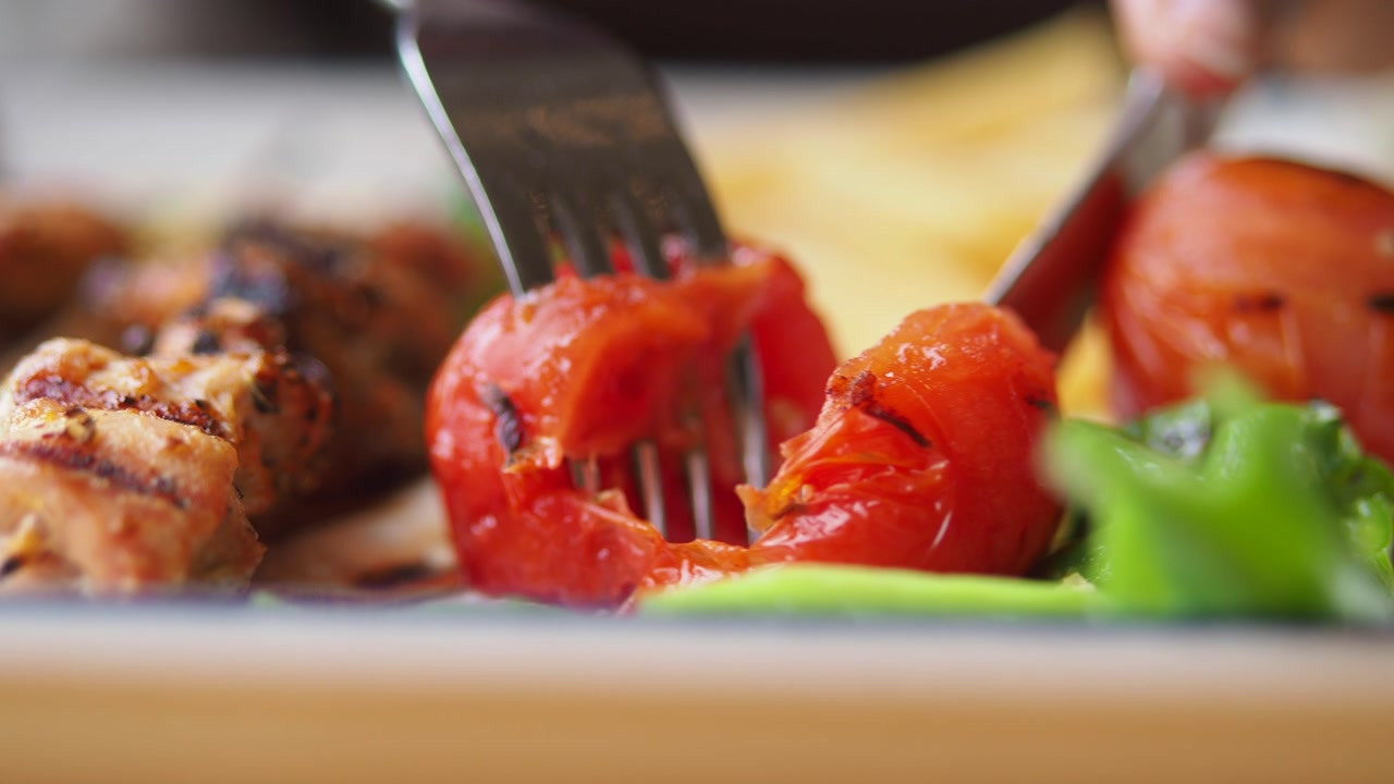 Close-up of a Grilled Tomato Being Cut with a Fork and Knife