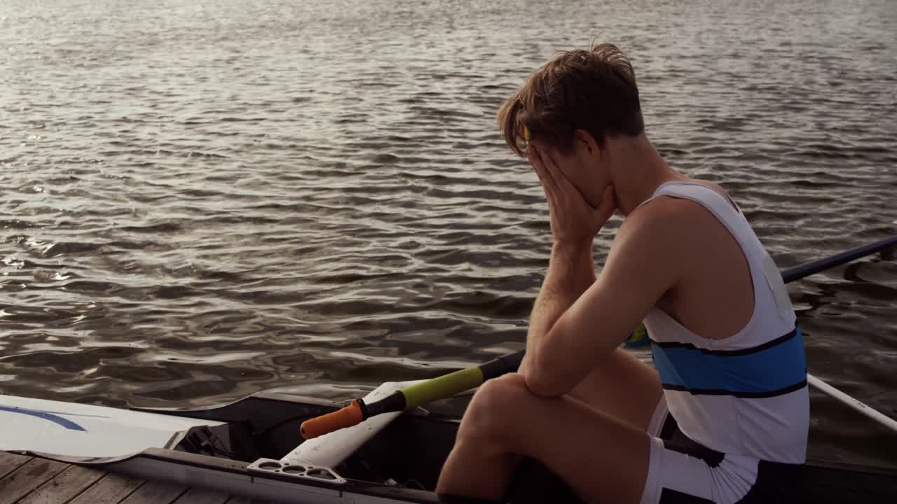 Male rower crying on the boat on the lake