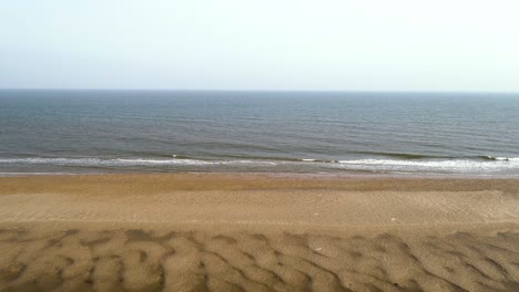 ascending drone shot of beach with waves and sand dunes in view with tide out and open water looking out to sea in norfolk, england