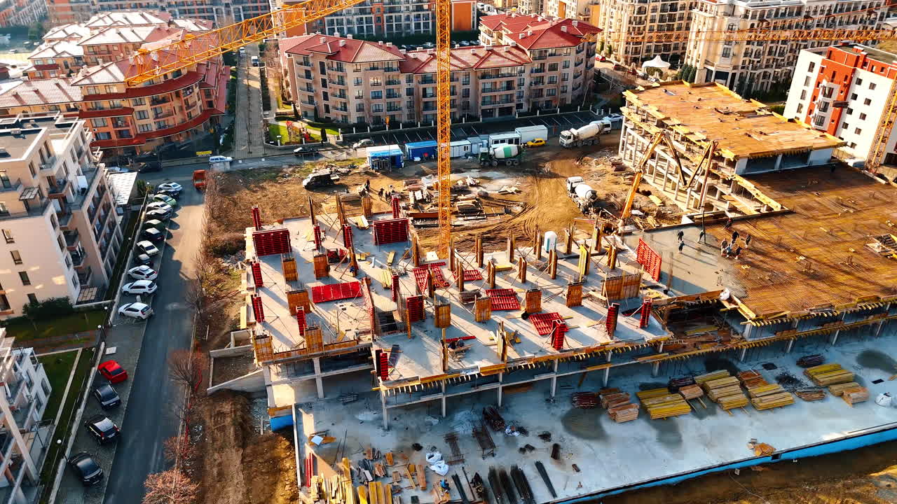 Workers and machinery on building frame at construction site. High angle shot of metal reinforcement and concrete formwork