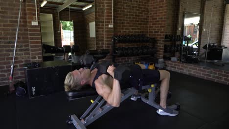 tattooed man in home gym shot from side man doing dumbbell bench chest press