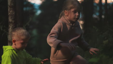 little children siblings walk through night wood together. scared boy and girl seek way to home in wild park in evening. small kids lost at forest area