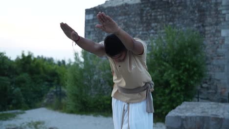 hombre indio estirando antes de hacer la meditación hatha yoga de pie ante las ruinas del castillo al amanecer