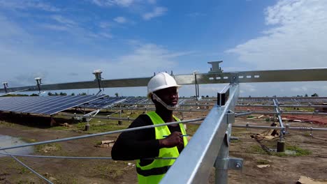 Schwarzer-Gambianischer-Afrikanischer-Männlicher-Ingenieur,-Der-Mit-Einem-Digitalen-Winkelmesser-In-Einem-Photovoltaikkraftwerk-In-Gambia,-Westafrika,-Die-Neigungswinkel-Neigungsmessung-Des-Solarenergie-Farm-Panel-Array-Rahmens-Durchführt