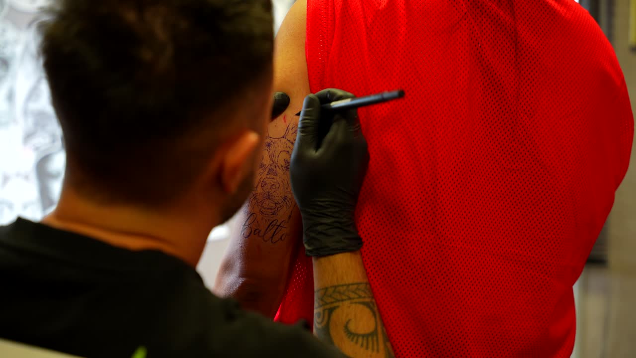 Tatuatore che prepara lo stencil di un ritratto di cane e del nome sul braccio superiore del cliente.
