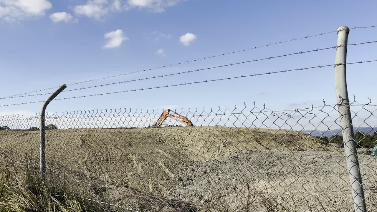 Excavator Performing Earthworks On A Construction Site Behind A Metal Barbed Wire Fence.