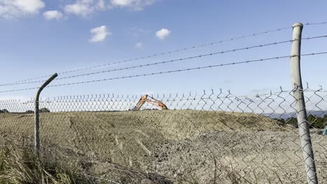 excavator performing earthworks on a construction site behind a metal barbed wire fence.