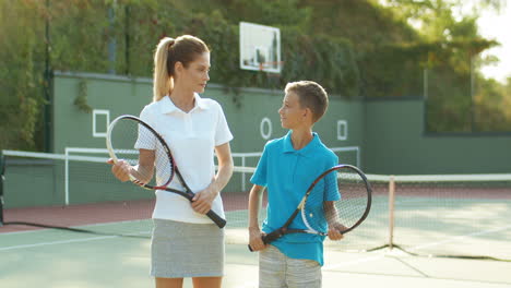 portrait of happy mother and her teen son smiling at the camera while standing at tennis court 1