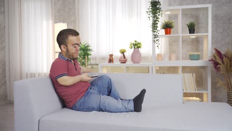 young dwarf man sitting on sofa at home and using smartphone.