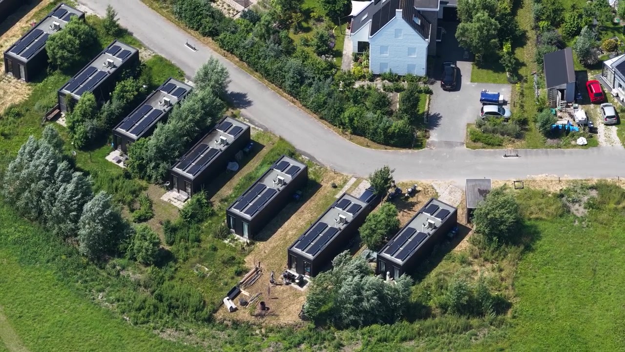 Luftfoto af små huse i en økolandsby, der viser selvforsynende livsstil, solpaneler, grønt boligdesign og et bæredygtigt samfundsmiljø