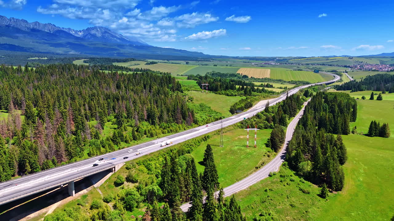 Cars run by the roads and freeway crossing the picturesque nature landscape. Slovakia countryside from aerial view. Tatra mountains at backdrop