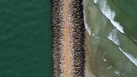 steinmauer, die einen ruhigen ozean von wellen trennt, die an einem strand krachen