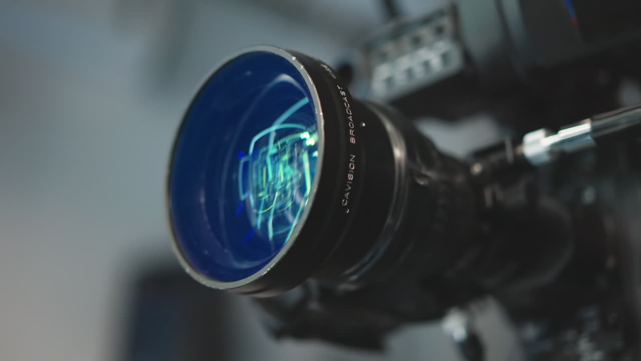 Close up cinema lens reflecting vibrant green and blue LED studio lights, revealing intricate glass elements and focus ring details, highlighting precision optics and coating