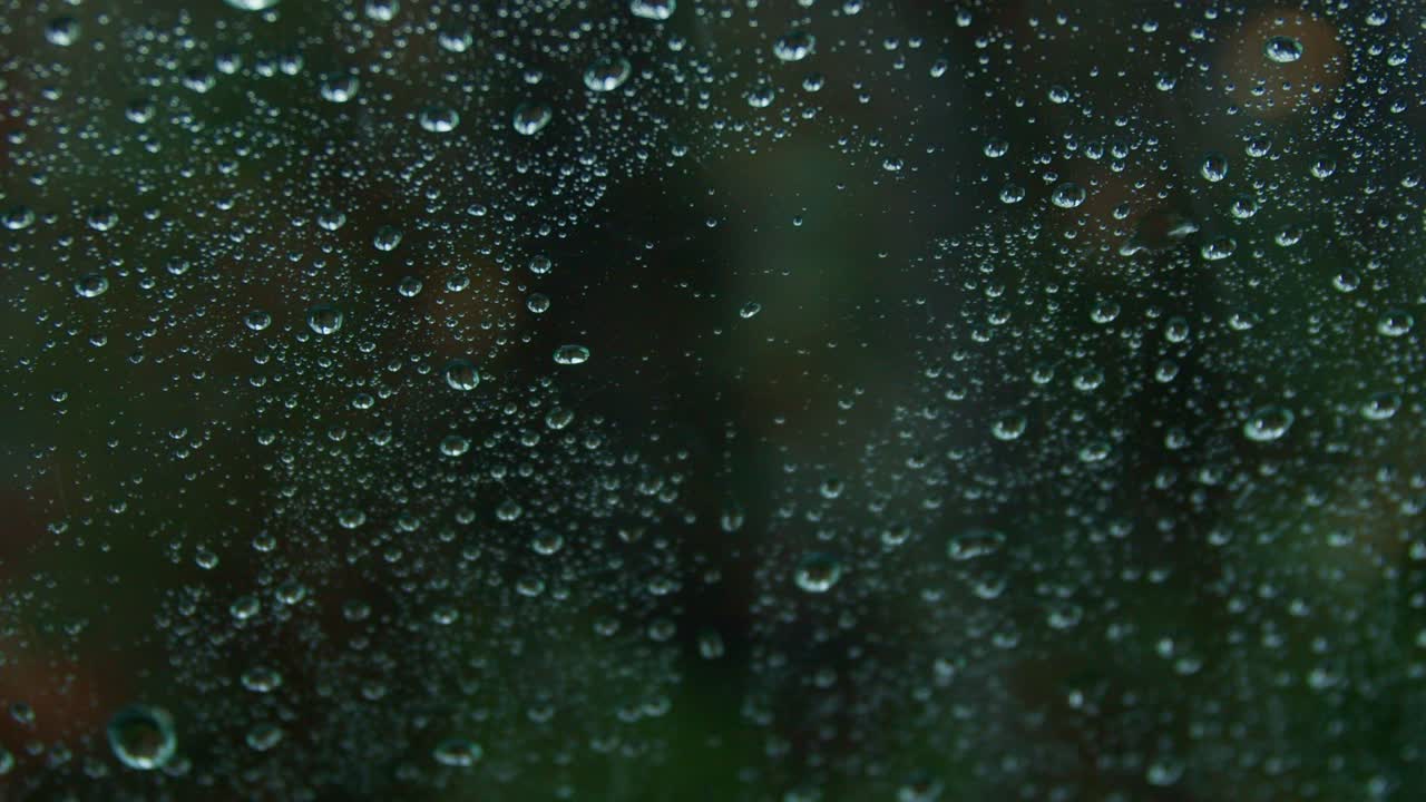 Raindrops falling on window glass, blurred forest background behind