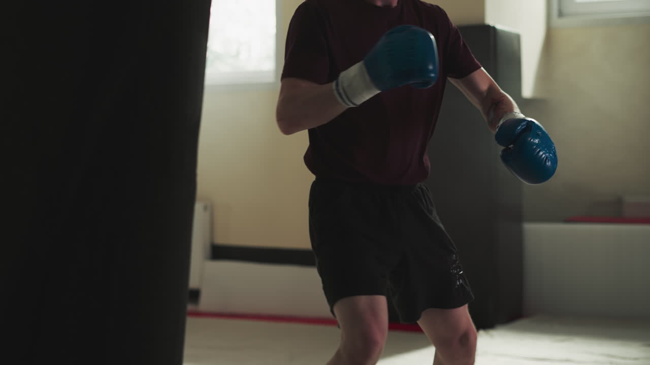 Man trains back kicks on punching bag in gym closeup. Combat master hits heavy equipment by legs in sports club slow motion. Stress reduce technique