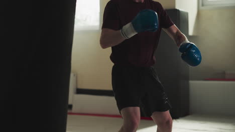 man trains back kicks on punching bag in gym closeup. combat master hits heavy equipment by legs in sports club slow motion. stress reduce technique