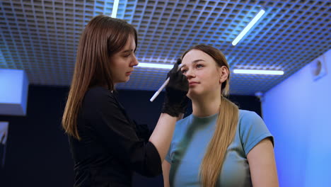 Marking the future eyebrow lines. Young girl is having beauty procedures and correction of brows in salon. Low angle view.