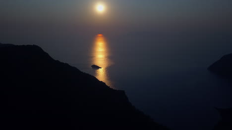 mountain ridge silhouetted by golden orange ocean sun beam sunset