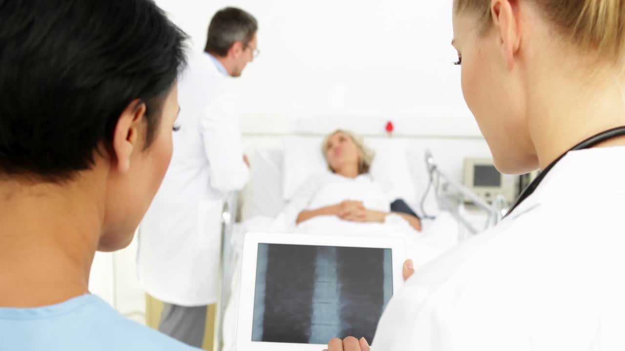 침대에서 아픈 환자 앞에서 태블릿에서  ⁇ 스레이를 연구하는 의사들