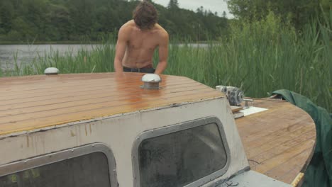 young topless carpenter walking to bow of wooden boat to start maintenance