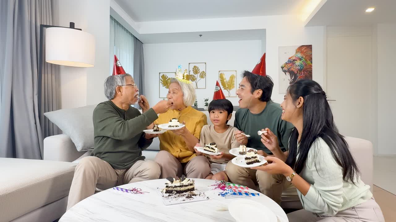Four generations share birthday cake in a bright living room, smiling and interacting warmly together