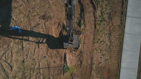 a drone pull away creating a bird’s eye view of a backhoe excavator beginning to dig a hole and basement for the foundation of a new house