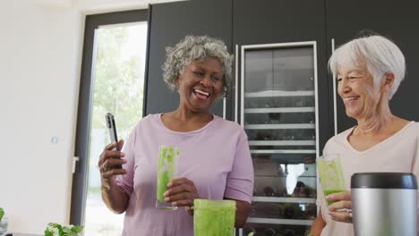 Happy-senior-diverse-women-drinking-healthy-drink-in-kitchen-at-retirement-home