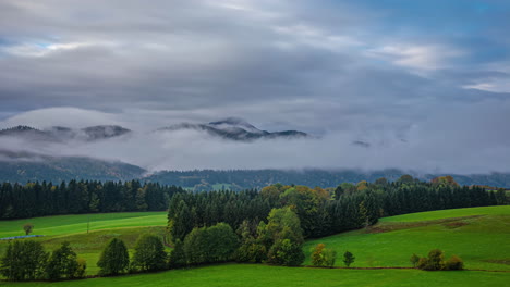 Timelapse-of-misty-clouds-gathering-at-mountain-base-above-forest-and-meadow-dispersing