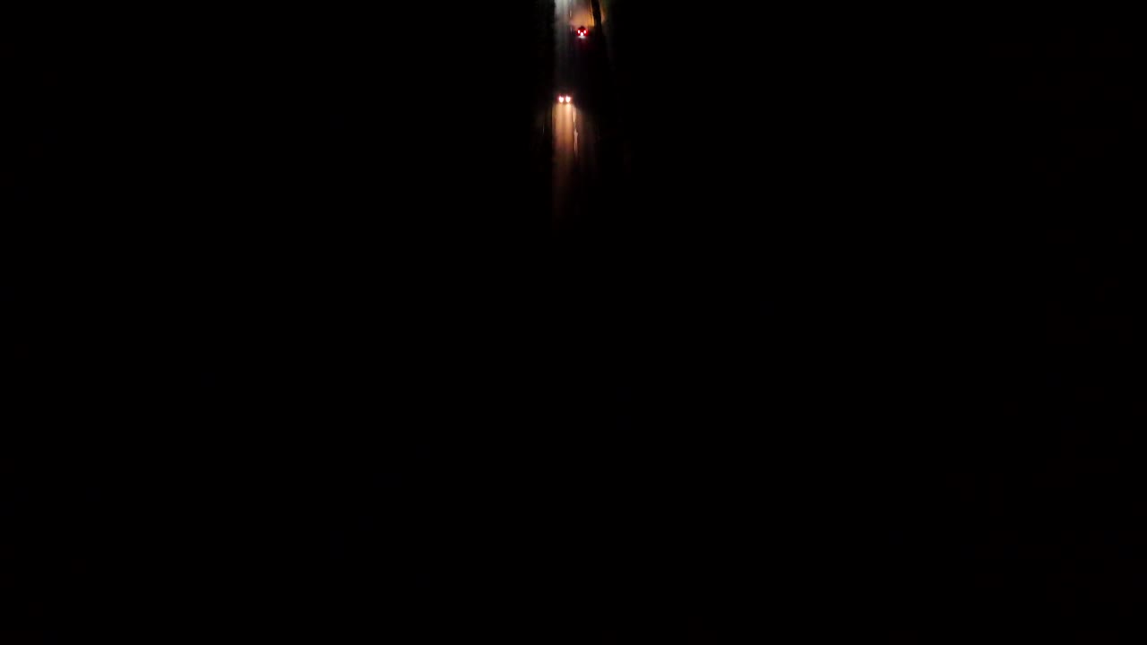 Traffic scene on american highway at night. Warm Lighting headlights in dark area of USA. Aerial top down shot. Vehicles on trip on rural street in american suburbia.